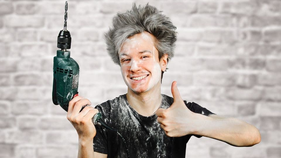 Schmutziger junger Handwerker mit Gipsflecken und Bohrmaschine