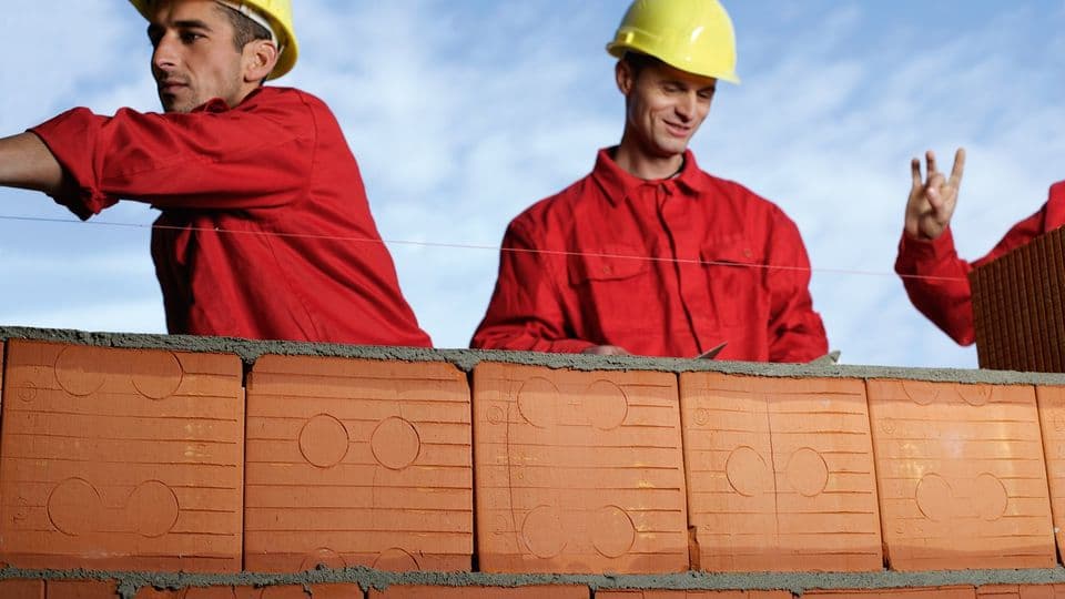 Drei Bauarbeiter hinter Ziegelmauer