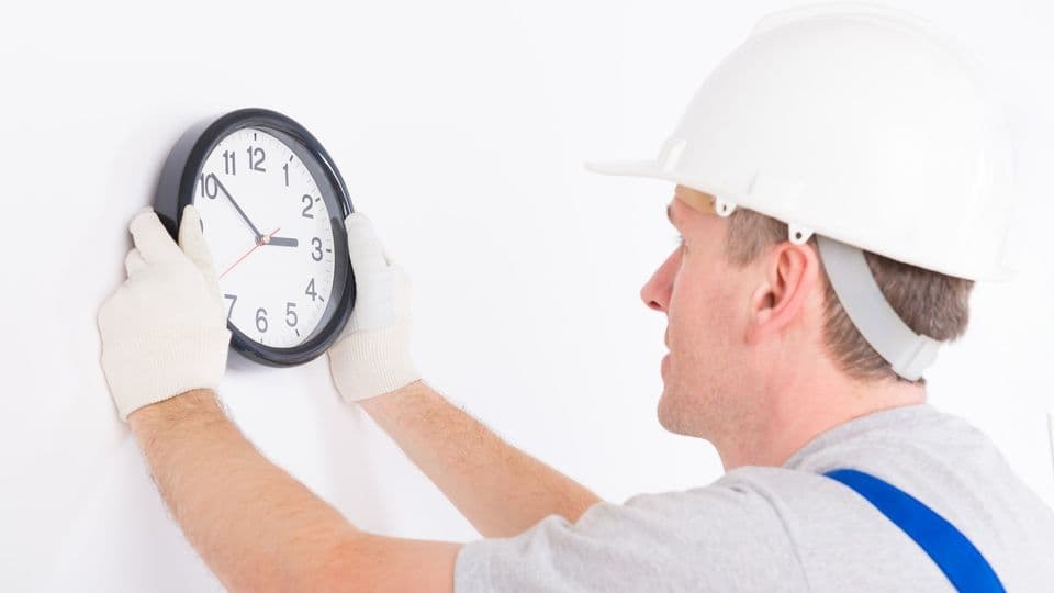 Arbeiter hängt Uhr an die Wand
Smiling man hanging wall clock wearing protective helmet