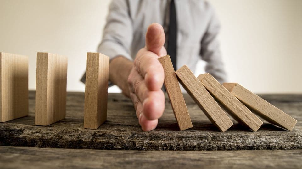Businessman halting the domino effect inserting his hand between falling and upright wooden blocks in a close up conceptual image.