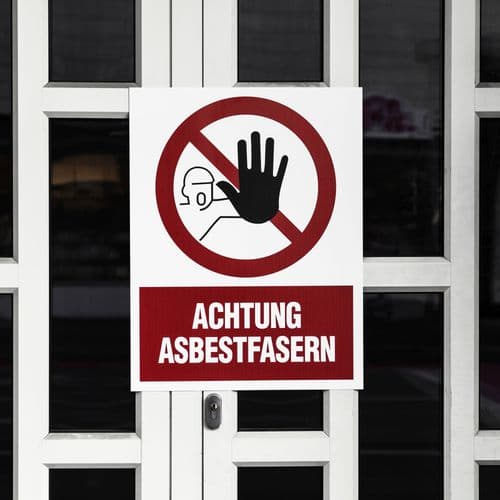 Weiße Haustür auf der ein Warnschild angebracht ist. Dort steht: "Achtung Asbestfasern".