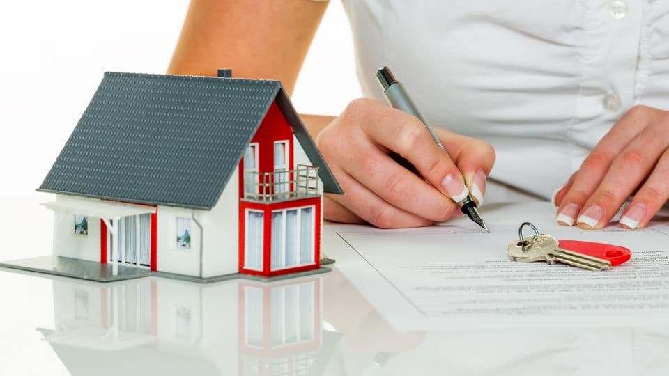 Eine Frau unterschreibt einen Kaufvertrag für ein Haus bei einem Immobilienmakler.