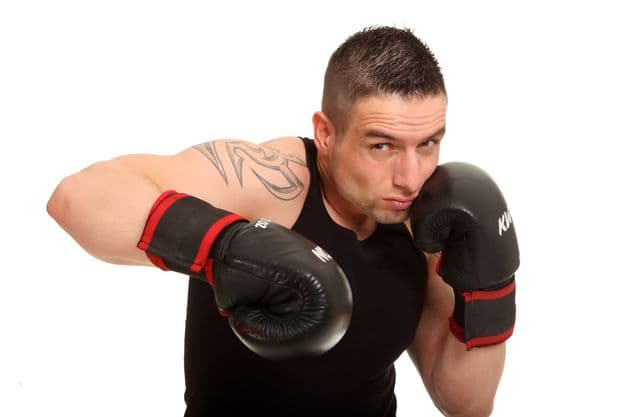 Junger tätowierter Sportler beim Versuch eines Schlages. Er schaut aggressiv in die Kamera