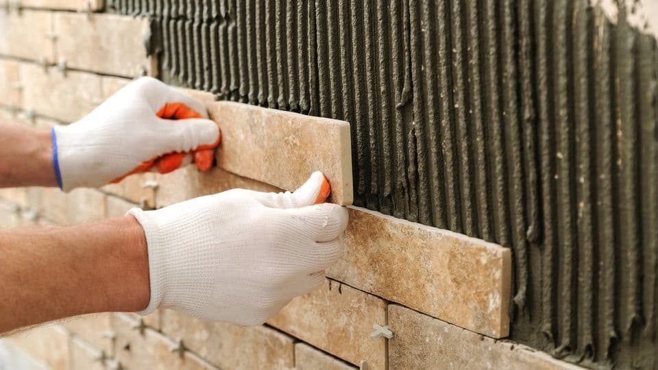Fliesenleger bringt Fliesen an einer Wand an.