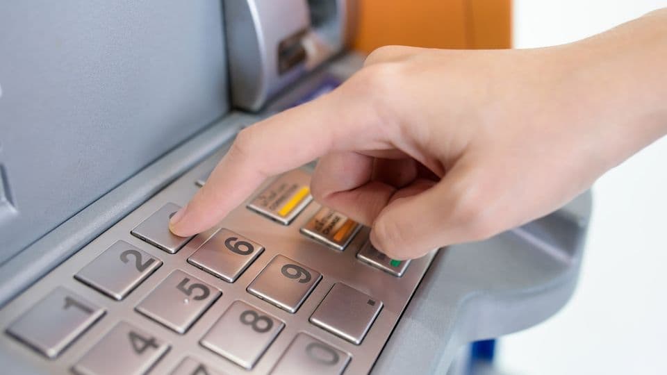 Junger Mann gibt am Bankautomaten seine PIN-Nummer ein, um Geld abzuheben.