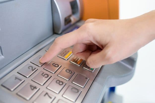 Junger Mann gibt am Bankautomaten seine PIN-Nummer ein, um Geld abzuheben.