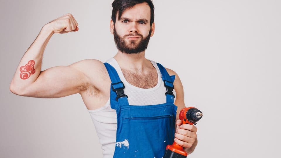 Handwerker in Arbeitskleidung spielt mit Musklen und zeigt Bohrmaschine