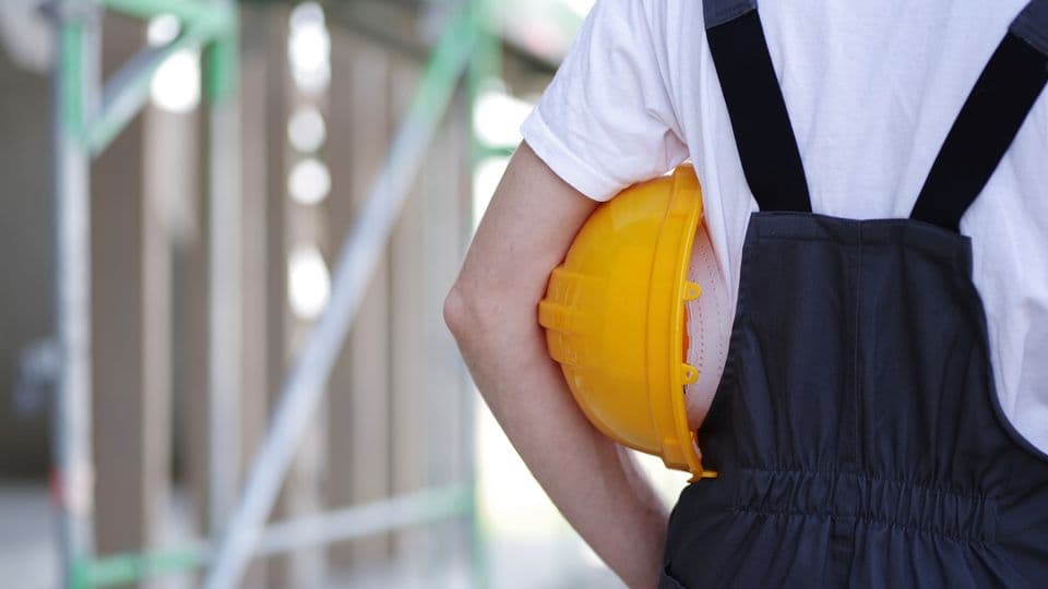 Handwerker im Blaumann hat einen gelben Helm unter den Arm geklemmt
