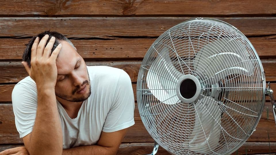 Mann wischt sich den Schweiß von der Stirn und sucht die Nähe zu einem Ventilator und sich abzukühlen.