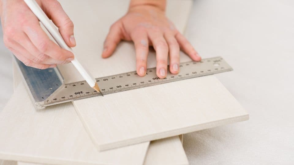 Holz wird abgemessen zum schneiden
Home improvement - handywoman measuring tile, focus on ruler