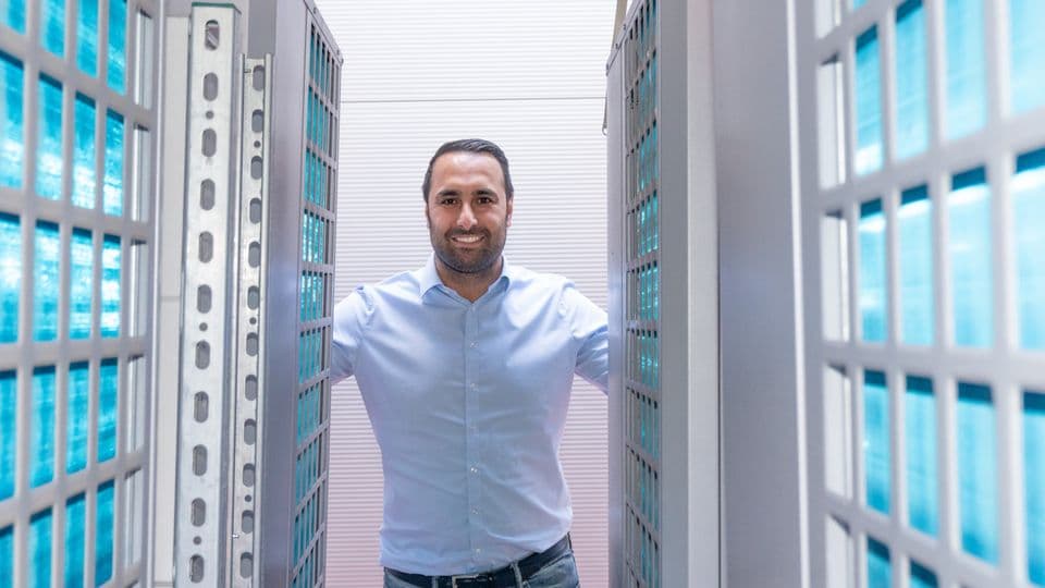Handwerksunternehmer Ahmet Düman mit einer 50-Kilowatt-Variante der mobilen Wärmepumpe. Blitzlicht lässt die Lamellen der Wärmetauscher blau aufleuchten.
