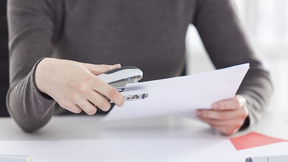 Eine Frau sitzt am Schreibtisch und tackert Papiere zusammen