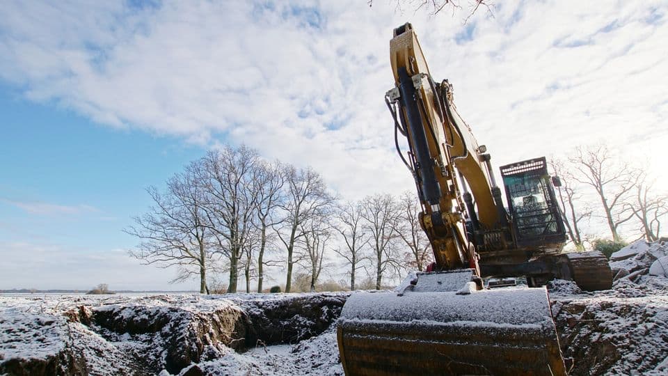 Baustelle im Winter mit Bagger, der von Schnee bedeckt ist.