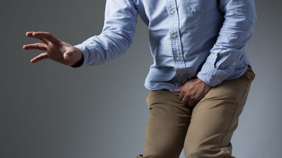 Mann kruemmt sich wegen Schmerzen im Genitalbereich