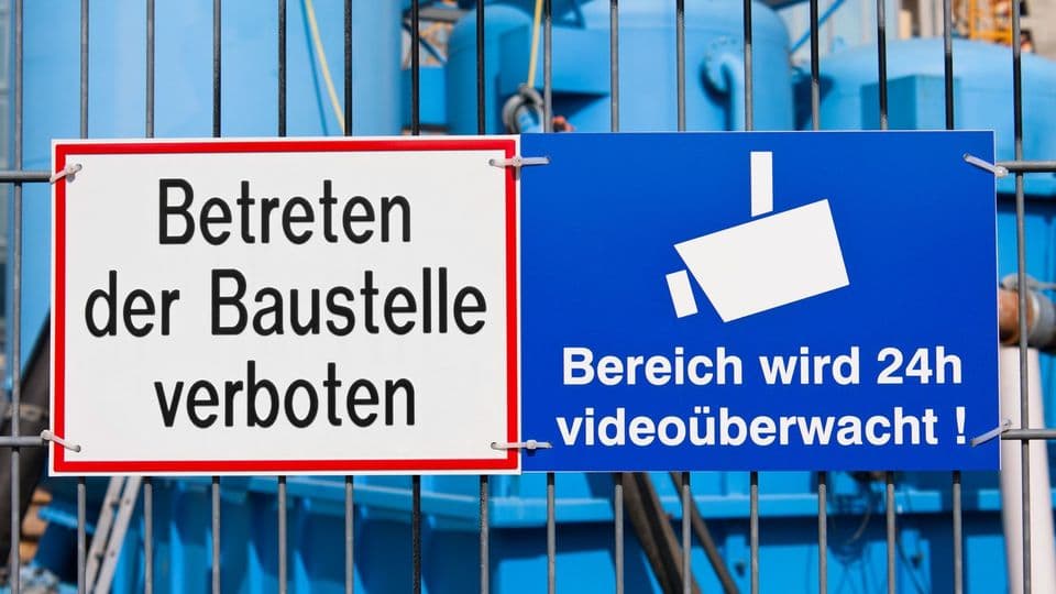 Schild am Bauzaun weist über permanente Videoüberwachung der Baustelle hin