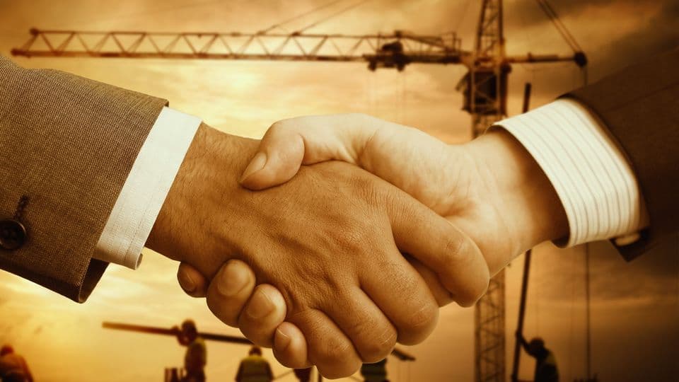 Zwei Männer reichen sich die Hand. Im Hintergrund ist eine Baustelle zu sehen.