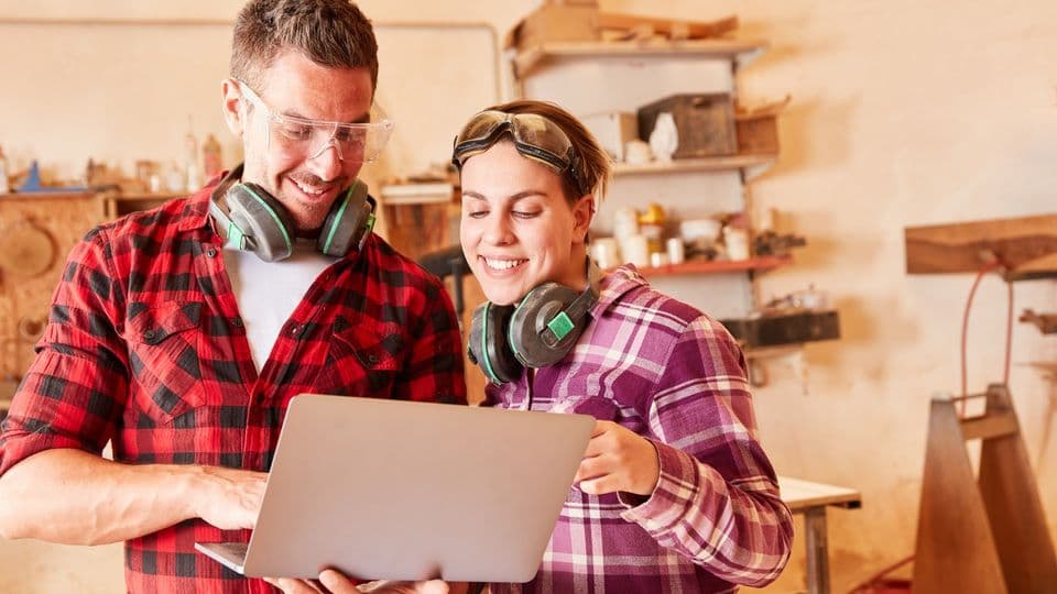 Junge Handwerker schauen zusammen auf einen Laptop Computer in der Werkstatt