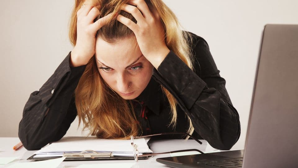 Eine Mitarbeiterin sitzt am Schreibtisch und ist mit ihrem Job unzufrieden. Sie rauft sich die Haare und starrt auf die Tischplatte.