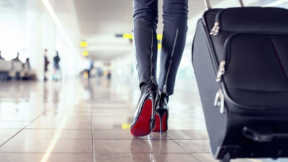 Eine Frau, die Highheels und Jeans trägt, zieht am Flughafen einen Koffer hinter sich her.