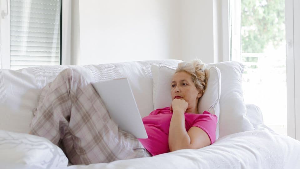 Eine Frau liegt in gemütlicher Kleidung auf dem Sofa und studiert aufmerksam einen Zettel.