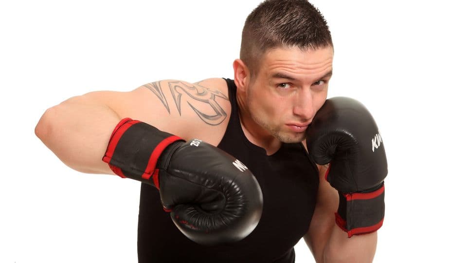Junger tätowierter Sportler beim Versuch eines Schlages. Er schaut aggressiv in die Kamera