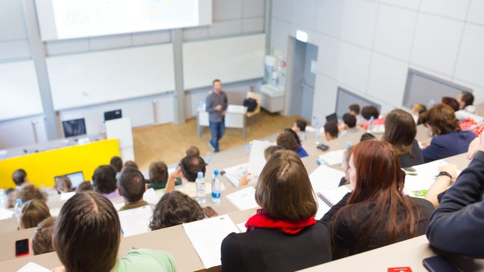Vorlesung an Uni
Speaker giving presentation in lecture hall at university. Students listening to lecture and making notes.