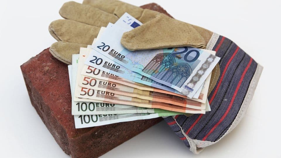 Diverse Geldscheine und ein Arbeitshandschuh liegen auf einem Geldschein.