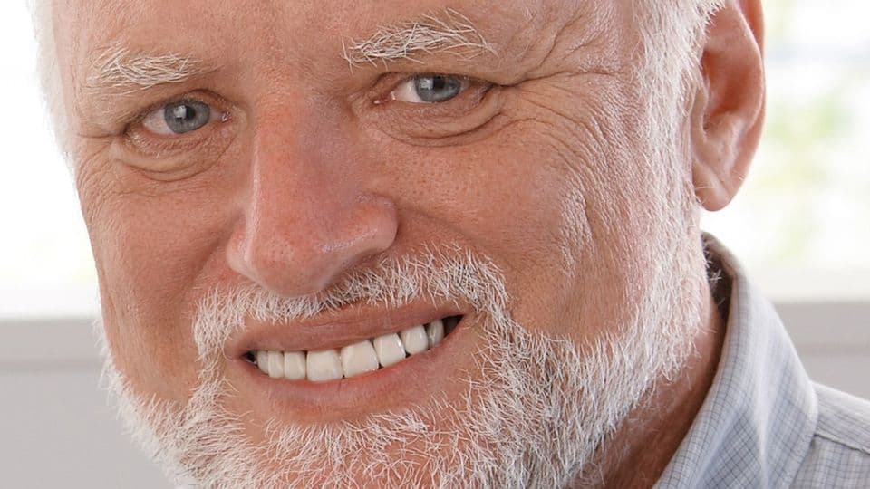 Mature man using computer, drinking tea, looking at camera, smiling.