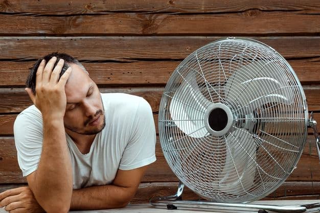 Mann wischt sich den Schweiß von der Stirn und sucht die Nähe zu einem Ventilator und sich abzukühlen.