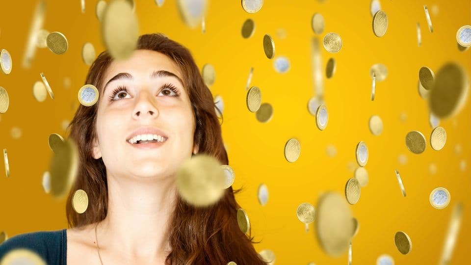 Frau blickt nach oben, woher ein Regen aus lauter Münzen kommt.