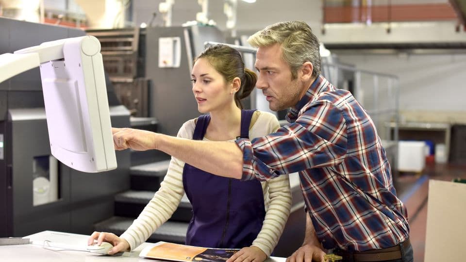 Ausbilder erklärt Mediengestalterin etwas in druckerei
Man working with apprentice in printing house