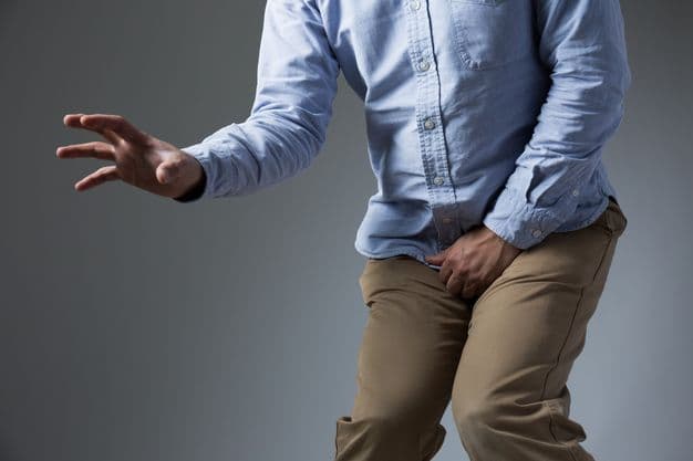 Mann kruemmt sich wegen Schmerzen im Genitalbereich